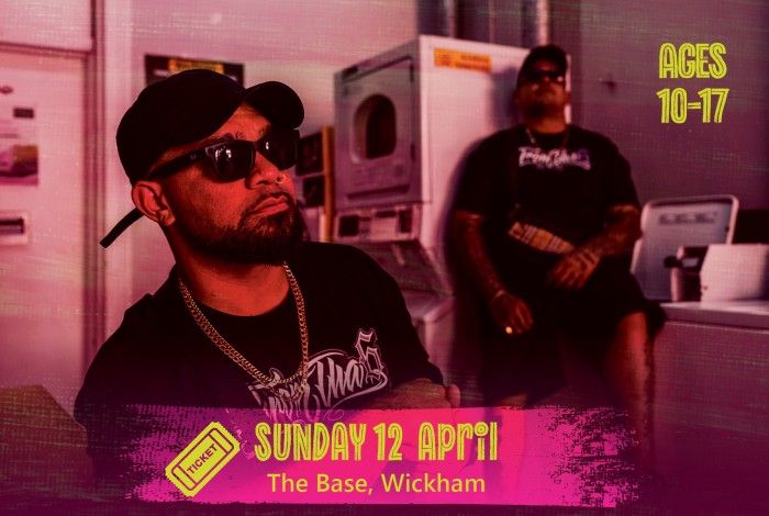 Two men wearing black caps and sunglasses sit in a laundromat setting with washing machines behind them. A pink banner reads “Sunday 12 April – The Base, Wickham,” and text on the right says “Ages 10–17.”